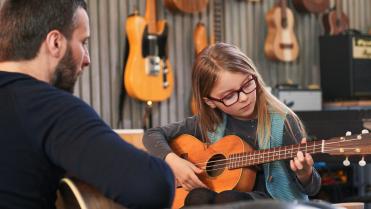 Mädchen spielt Gitarre mit Musiklehrer